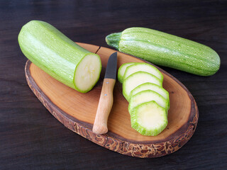 Slicing zucchini on wooden board over dark table