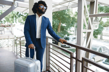 Black man in formal suit with packed suitcase entering hotel door