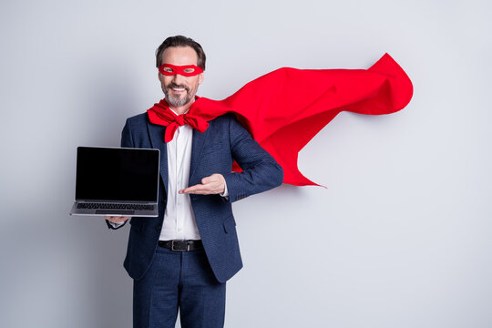 Photo of cheerful aged mature business guy superhero costume hold laptop showing new device sale manager modern user wear suit red face mask cloak flying isolated grey background