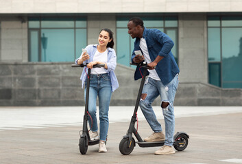 Fototapeta na wymiar Couple having ride on motorized kick scooters, holding phones