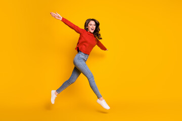 Full body photo of attractive pretty lady jumping high up spread arms like wings plane flight walking street crazy wear red sweater jeans shoes isolated yellow color background