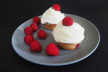 raspberries and two gluten-free cupcakes with mascarpone cream and cream on a gray round plate on a black background