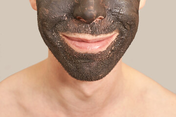 Black Clay Mask on Guy Face. Cosmetology man portrait with mud healthy scrub. Coal nature eco...