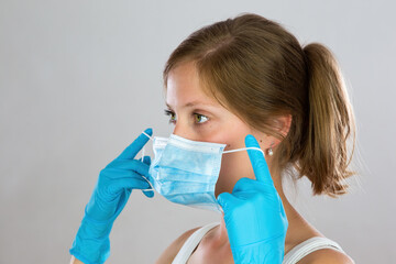 Young woman with blond hair putting on face mask from side view. Portrait of female wearing blue...