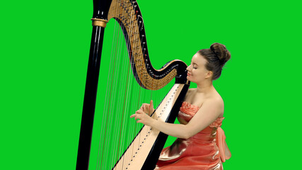Young beautiful lady in dress playing harp on green screen background