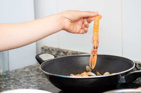 Hand of a woman adding a shrimp to the cut in her home kitchen