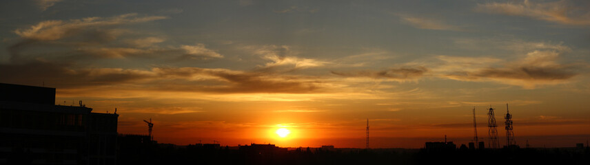Color photograph of the city against the sunset. The Yellow Sun sets over the horizon. Beautiful clouds in the sky. Smooth natural gradient from blue to red. End of the day.