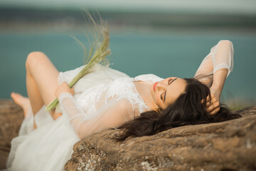 beautiful young female with makeup and hairstyle in a gentle wedding peignoir lies on the stones outdoors