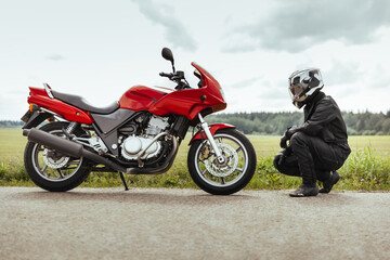 Man motorcyclist in helmet sits in front of a motorcycle and looks at it