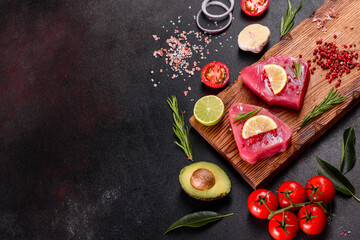 Obraz na płótnie Canvas Fresh tuna fillet steaks with spices and herbs on a black background