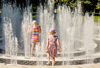 Children playing in water splashing fountain in public park, having fun on warm sunny summer day.