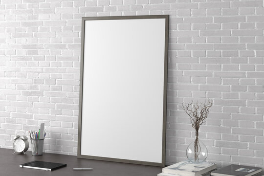 Vertical poster frame mockup on the black table of home studio workspace with white brick wall. Side view, clipping path around poster picture.