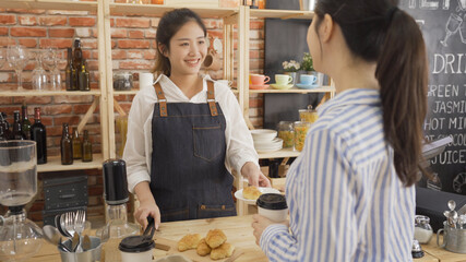 Barista serving cup of coffee to go and delicious croissant for customer at counter in small cafe shop. female owner serving breakfast to client in coffeehouse. waitress smiling to office lady guest