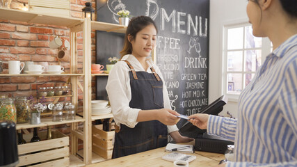 office lady customer paying on credit card through payment terminal in cafe. waitress taking recharge card from client and using tablet. young girl barista working in counter of coffee shop.