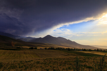 Thundercloud in the mountains. The beginning of the rain. Heavy cloud against the blue sky and bright sun. Natural background. Overcast weather