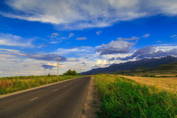 Beautiful summer landscape. Mountain country road among green hills. Lush green hills, high mountains. Spring flowering grass.