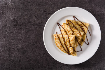 Sweet crepes with chocolate syrup on black background. Top view.Copy space