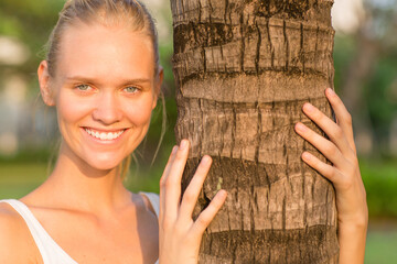Beautiful happy female model smiling with teeth at the camera next to a tree trunk in the nature. Beauty, nature and wellness.