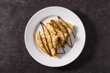 Sweet crepes with chocolate syrup on black background. Top view