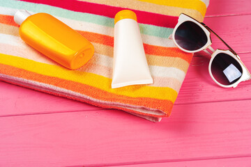 Colorful striped towel with sunscreen cream and sunglasses on pink wooden background