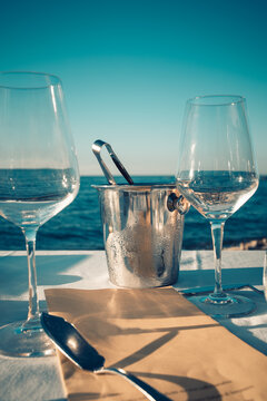 Expensive Dinner At Sunset On A Beach Restaurant With Amazing Sea View. Close Up Of Ice Bucket With Tongs And Empty Wine Chalices And Brown Paper Menu. Romantic Atmosphere.