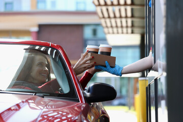 Woman in convertible car picks up tea and coffee in Mcdrive. Fast and safe service in restaurants...