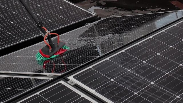 Panning shot of a worker cleaning solar panels on a flat roof with osmosis water