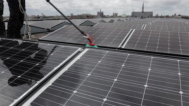 Worker cleaning solar panels on a flat roof spraying osmosis water