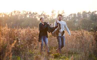 Beautiful young family with small son on a walk in autumn nature.
