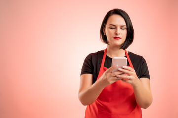 Woman employed at supermarket with red apron and black t-shirt holding smartphone, texting messages