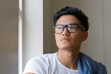 Face of handsome Asian man with eyeglasses looking outside the window