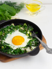 Green shakshuka. Fried eggs with fresh arugula, green onions, dill in a pan
