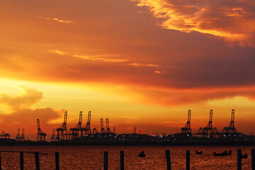 cranes on seaport and sunset red orange sky and fishing boats are on sea