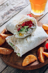 Doner kebab or shawarma. Grilled chicken in pita bread with tomatoes, corn and green salad on wooden board. Rustic wooden background. Middle Eastern food, arabic fast food concept