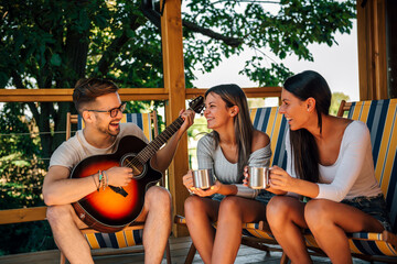 Young man playing guitar to a two female friends.