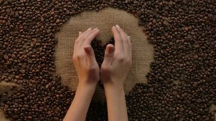 Woman's hands holding a heart shape coffee beans with care,enjoyment, and passion coffee. Concept for love of coffee and caffeine. Background with grains and burlap, flat lay