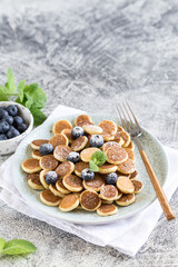Tiny pancakes for breakfast. Cereal pancakes with blueberries in plate on grey background. Trendy food. Copy space for text or design