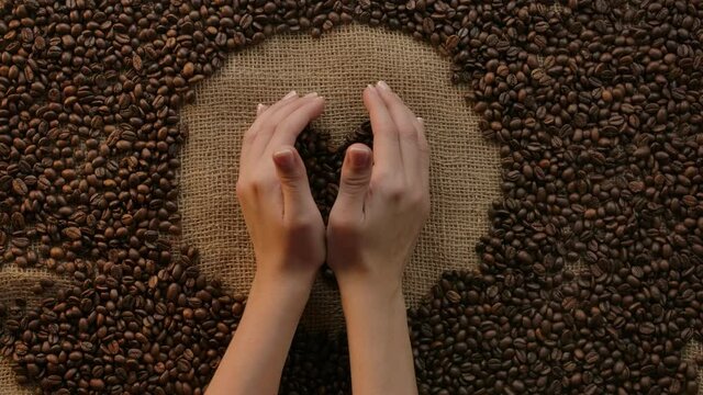 Woman's hands holding a heart shape coffee beans with care,enjoyment, and passion coffee. Concept for love of coffee and caffeine. Background with grains and burlap, flat lay