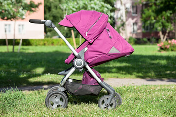 Baby pushchair is on green meadow in summer sunny park, side view, infant perambulator series