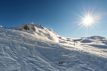 Scenic view of snow covered alpine mountain on bright sunny winter day. Snowcapped peaks against vibrant shining sun on blue clear sky. panoramic nature landscape