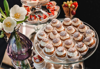 Wedding dessert, macaroons, meringues, cupcakes, muffins, cakes and sweetness on holiday background with flowers. Candy bar