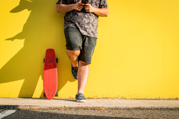 Curvy man with skateboard and yellow background looking at the mobile phone.