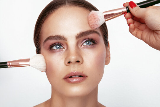 Make up process. Beautiful Model looking up when make up artist applies cosmetic products on her face.