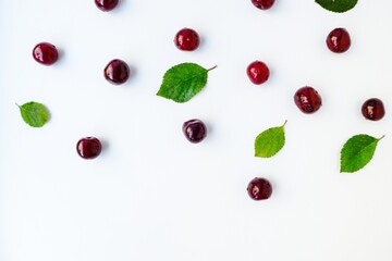 Bright red juicy ripe cherry with green leaves scattered on a white background.