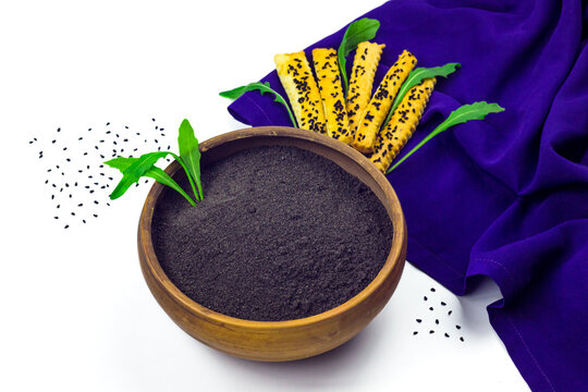 Black cumin flour in ceramic bowl, cumin seeds, crispy breadsticks or grissini, arugula and violet cloth isolated on white background
