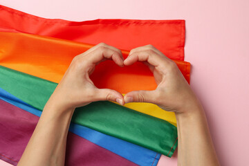 Heart made of female hands on pink background with LGBT flag