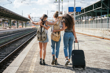 Three young friends women at the station walking and waiting train for their trip in summer with face mask for protection by infection from Coronavirus, Covid-19 - Millennials having fun together - 366285607