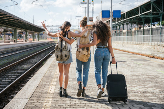 Three young friends women at the station walking and waiting train for their trip in summer with face mask for protection by infection from Coronavirus, Covid-19 - Millennials having fun together