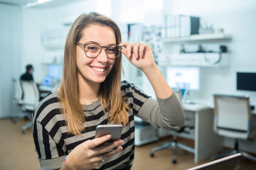 Segretaria, bionda è seduta sorridente nella sua postazione di lavoro mentre tiene in mano un cellulare  nel suo ufficio 