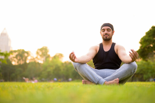 Young handsome bearded Indian man meditating at the park